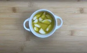 White bowl with garlic cloves in olive oil on wooden background. Perfect for cooking and flavoring dishes.